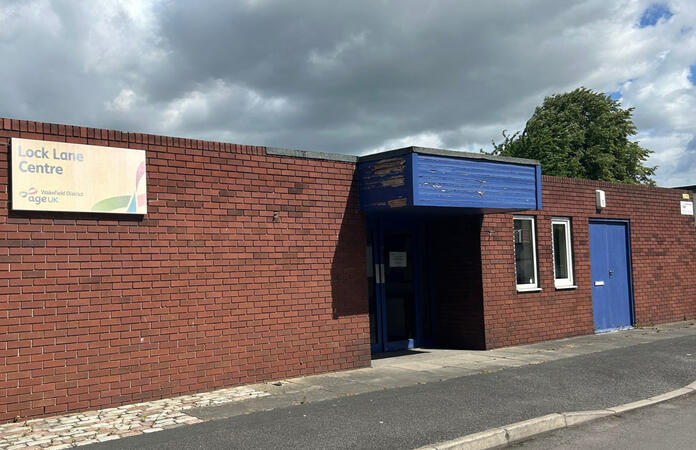 Front of Lock Lane Centre building in Castleford. Brown bricks with faded blue entrance and faded Age UK Wakefield District sign